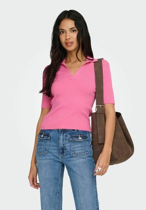 Femme portant un haut à manches courtes côtelé rose, un jean bleu avec des poches avant, et portant un grand sac à bandoulière marron.