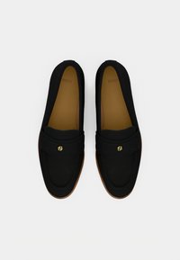 Pantofi loafer negri din material textil cu textură fină, prevăzuți cu o curea decorativă și un mic detaliu auriu, pe o talpă maro.