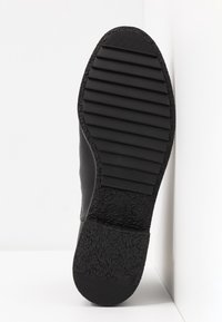 Suela de zapato negra con una superficie de goma texturizada y ranuras horizontales para tracción, y un borde liso y redondeado.