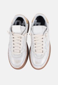 Zapatillas deportivas de cuero blanco con un acabado brillante, detalles perforados, cordones crema y una suela de goma marrón en forma redondeada.