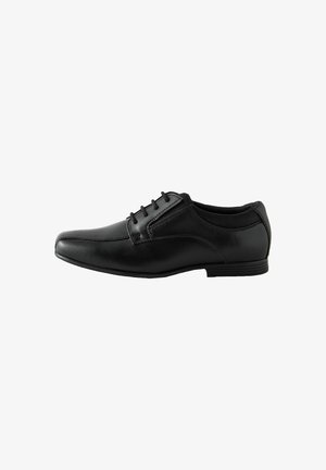 Zapato de vestir de hombre de cuero negro con cordones y tacón bajo, mostrado de lado sobre un fondo blanco.