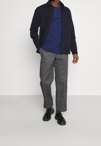 Navy button-up shirt layered over a blue t-shirt, paired with grey trousers and black shoes. Smooth texture, casual design, and relaxed fit.