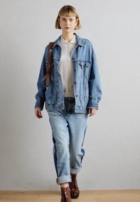 Veste en denim à coupe décontractée, couleur bleu clair, avec deux poches avant et une fermeture à boutons. Associée à un jean bleu clair et des bottes marron.