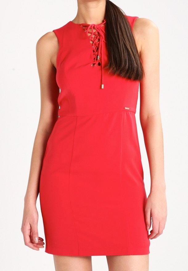 Femme portant une robe rouge sans manches avec un détail lacé au niveau du décolleté et une couture haute à la taille, debout les bras détendus.