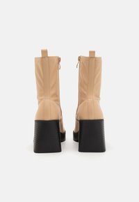 Beige high-heeled ankle boots with a shiny finish, textured black block heels, and side zippers for easy wear.