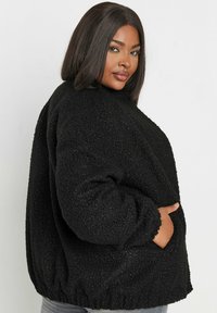 Czarna puszysta kurtka wykonana z teksturowanej tkaniny, o luźnym kroju, z prążkowanymi mankietami i marszczonym dołem. Posiada boczne kieszenie dla dodatkowej funkcjonalności.