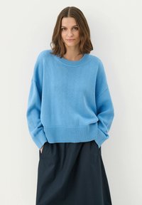 Helleblaue Strickjacke mit Rundhalsausschnitt, geripptem Saum und überschnittenen Schultern, kombiniert mit einem dunklen Rock. Weiche Textur.