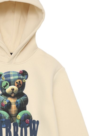 Felpa color crema con una grafica di un orso con pelliccia a scacchi e dettagli colorati sui bottoni. Sotto, in caratteri grandi, c'è scritto "BROW."