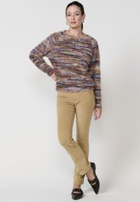Mehrfarbiger strukturierter Pullover mit langen Ärmeln, kombiniert mit beigen Slim-Fit-Hosen und schwarzen spitzen High Heels.