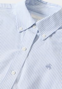 Striped button-up shirt in light blue and white, made of cotton. Features a classic collar, white buttons, and a small embroidered logo.