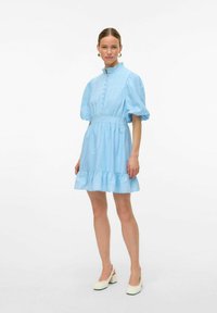 Svetlo modra kratka obleka z visokim ovratnikom, napihnjenimi rokavi, sprednjimi gumbi in nagubanimi robovi. Iz bombažne tkanine z vezenimi detajli.