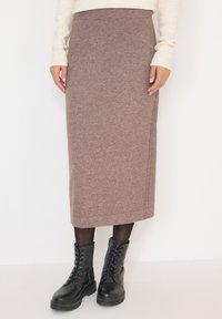 Jupe midi en tricot marron avec une taille côtelée et des détails sur les coutures latérales, associée à des bottines noires à lacets et des collants opaques.