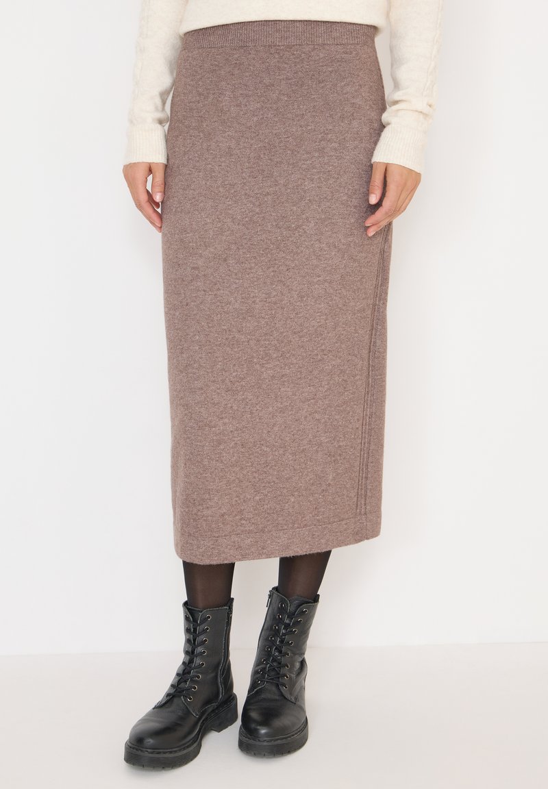 Jupe midi en tricot marron avec une taille côtelée et des détails sur les coutures latérales, associée à des bottines noires à lacets et des collants opaques.