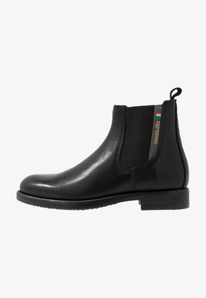 Botín Chelsea de cuero negro con paneles laterales elásticos, puntera redondeada y un asa. Presenta un acabado texturizado y un sutil detalle de logo.