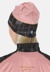 Roze beanie met een zwarte patroonband, voorzien van een kleine Zweedse vlag. Materiaal lijkt zacht, met een nauwsluitende vorm en gedetailleerde stiksels.
