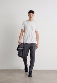Pantaloni sport gri, tricou alb și adidași negri. Pantalonii au o textură fină cu un detaliu subtil de dungi.