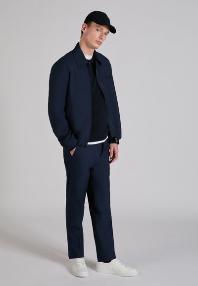 Navy bomber jacket with a smooth texture, paired with a navy sweater and coordinating trousers. White sneakers complete the outfit.