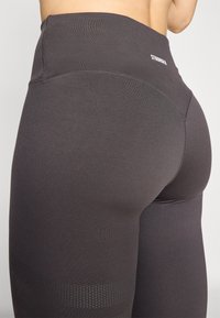 High-waisted leggings in dark gray, made of smooth fabric with a textured panel design and a white logo at the back.