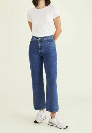 Camiseta de manga corta a rayas rosa claro y blanca, combinada con jeans de pierna ancha de denim azul de cintura alta. Zapatillas deportivas blancas.