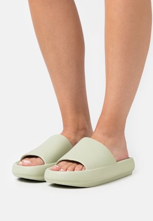 Sandales slip-on vert clair avec un dessus texturé et une semelle épaisse. Design ouvert avec des larges brides pour le confort et un enfilage facile.