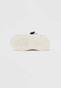 Talpă albă de cauciuc pentru încălțăminte, cu suprafață texturată, având un model de diamant și perforații circulare pentru aderență. Numele mărcii este imprimat.