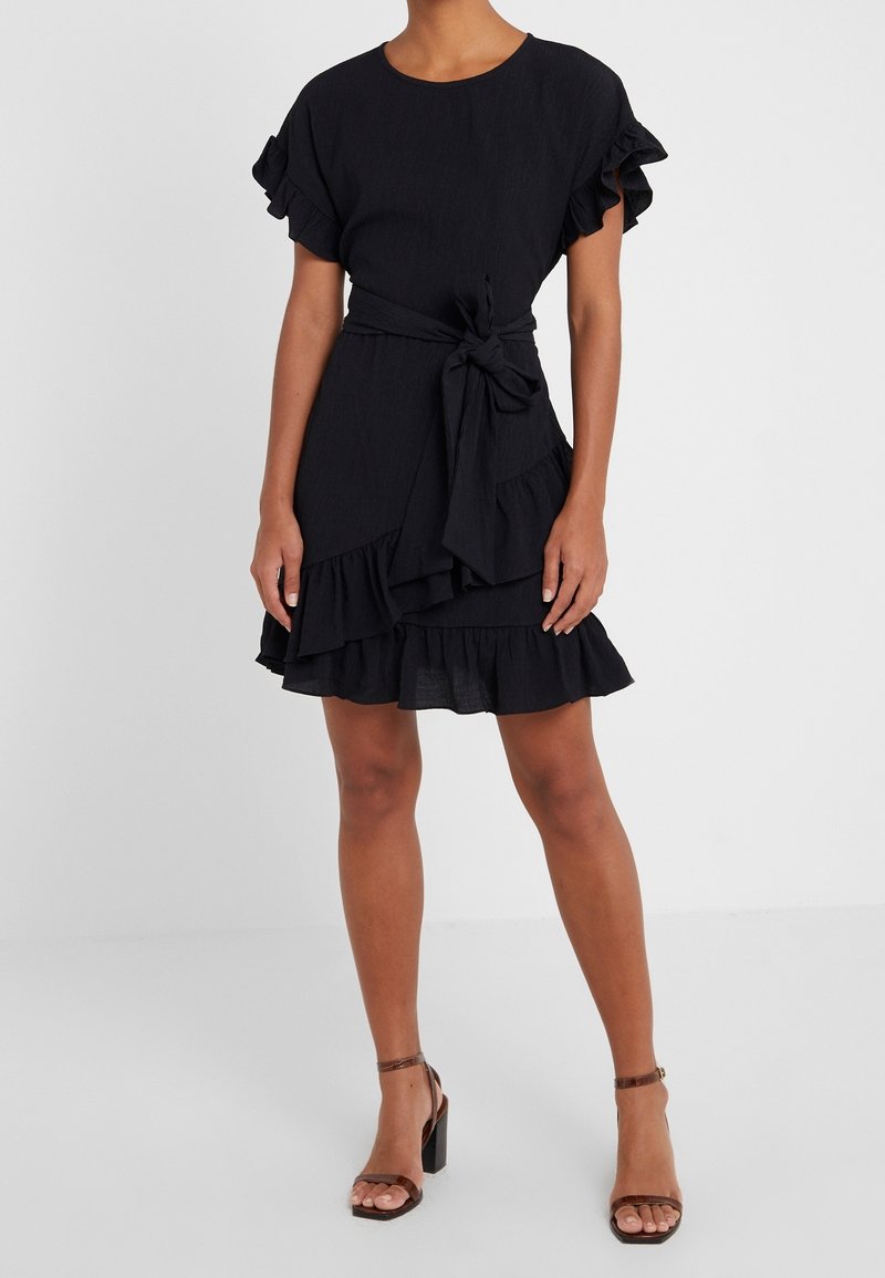 Schwarzes Kleid mit kurzen Rüschärmeln, einem Bindegürtel und einem mehrlagigen Rüschensaum. Hergestellt aus strukturiertem Stoff, hat es einen runden Ausschnitt.