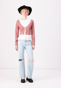Pöttyös piros és fehér kockás cropped kardigán, megkötővel, egy fehér póló fölött; világos kék kiszakadt farmernadrággal és fekete cipővel párosítva.