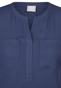 Marineblaue Bluse mit rundem Ausschnitt, mittigem Schlitz an der Vorderseite, zwei Brusttaschen und einem strukturierten Paneel mit dezenten Verzierungen.