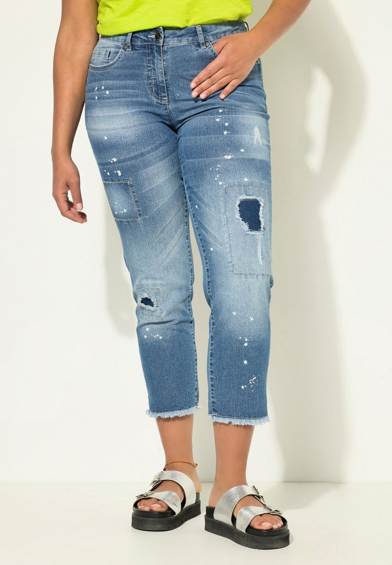 Jeans cortos de mezclilla azul con detalles desgastados, lavado deslavado y dobladillos deshilachados. Combinados con sandalias plateadas con suela gruesa y hebilla.