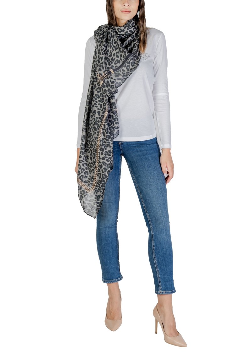 Sciarpa con stampa leopardata in tessuto trasparente, drappeggiata elegantemente, con un dettaglio in catena dorata, abbinata a una maglietta bianca e jeans blu.