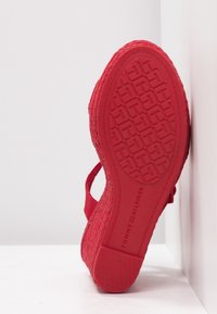 Sandale plateforme rouge avec semelle extérieure en caoutchouc texturé et dessus en tissu tissé. Dispose d'une bride ajustable et d'une semelle à motifs pour une meilleure traction.