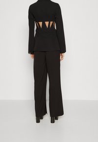 Czarna dopasowana marynarka z długimi rękawami, z wycięciami w kształcie trójkątów z tyłu. W połączeniu z szerokimi czarnymi spodniami i błyszczącymi szpilkami.