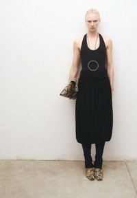 Crna halter majica s uskim strukom, lepršava crna suknja i cipele s uzorkom zmijske kože. Drži clutch torbicu od zmijske kože; dugi okrugli ogrlica.
