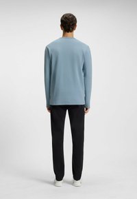Long-sleeve, light blue ribbed shirt with a round neck, paired with black trousers and white sneakers. Simplistic design and soft texture.
