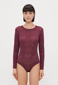 Hosszú ujjú body sötét bordó színben, texturált zebra mintával, kerek nyakkivágással és testhez simuló fazonnal.