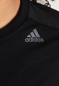Black short-sleeve shirt featuring a round neckline, smooth texture, and grey Adidas logo on the left side of the chest.