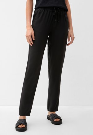 Black, lightweight, elastic-waist pants with a drawstring tie. Smooth texture and tapered fit, paired with black slide sandals.