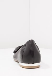 Chaussure plate en cuir noir avec un bout arrondi, un accent en nœud sur le devant et un détail en métal argenté sur le talon bas.