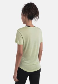 Camiseta de manga corta verde claro con escote redondo, textura suave y dobladillo ligeramente curvado, llevada sobre leggings negros.
