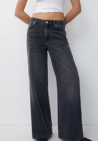 Wide-leg jeans in dark gray denim, featuring a high waist, front pockets, and a button closure. Smooth texture with subtle fading.
