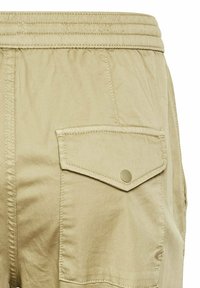 Beige Cargo-Shorts mit einem elastischen Bund, ausgestattet mit einer großen Gesäßtasche mit einem Knopfverschluss und sichtbaren Nähdetails.