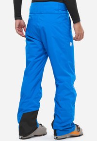 Blaue Skihosen mit flachem Bund, Seitentaschen und schwarzen verstärkten Säumen. Hergestellt aus wetterfestem Material; glatte Textur.