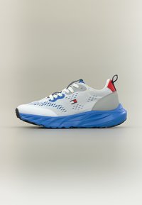 Λευκό αθλητικό παπούτσι με μπλε σόλα, γκρι λεπτομέρειες και κόκκινη φτέρνα. Διαθέτει επάνω μέρος από δίχτυ με οπές αερισμού και υφή στη λαστιχένια σόλα.