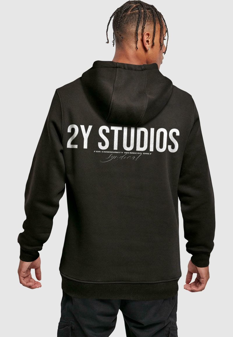Felpa nera con cappuccio, caratterizzata da grande testo bianco "2Y STUDIOS" sulla schiena, insieme a ulteriore testo più piccolo sottostante.