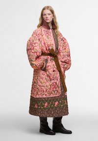 Vyšívaný růžový kabát s květinovým vzorem, přes veliké rukávy, hnědý pásek a kontrastní zelený lem. Teplý a texturovaný design.