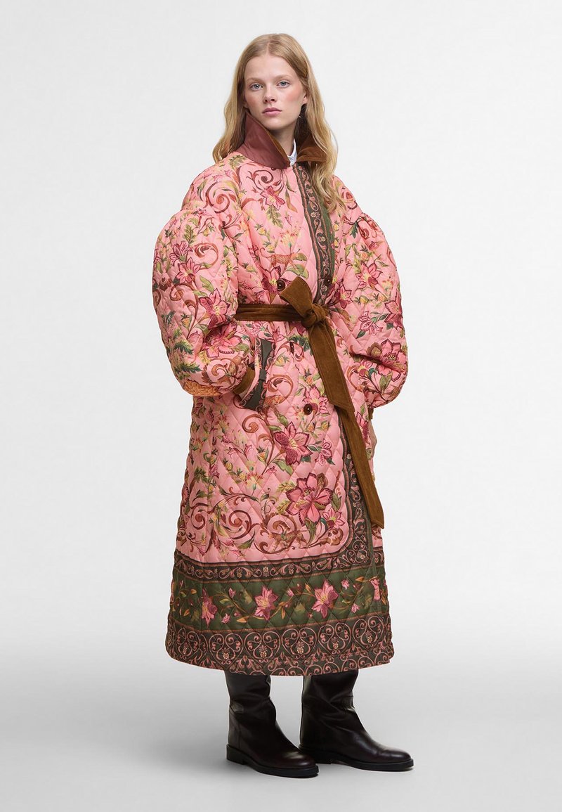 Vyšívaný růžový kabát s květinovým vzorem, přes veliké rukávy, hnědý pásek a kontrastní zelený lem. Teplý a texturovaný design.