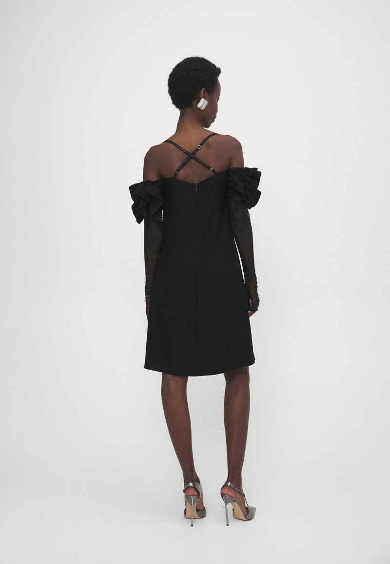 Czarna sukienka z odkrytymi ramionami, zdobiona falbanami i dopasowanym krojem. Posiada zamek błyskawiczny oraz krzyżujące się paski na plecach.