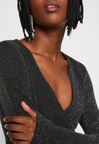 Svart, ribbadan långärmad topp med djup V-urringning, med silvertråd för textur och en figurnära silhuett.