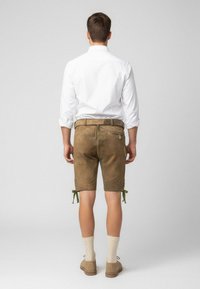 Pantaloni corti di pelle marrone con lacci verdi all'orlo, indossati con calze beige fino al ginocchio e scarpe marroni, visti da dietro. Camicia bianca visibile.