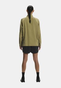 Zöld dzseki magas gallérral, hosszú ujjakkal és laza szabással, fekete nadrágpóttal párosítva. Sima textúra, minimalista dizájn.